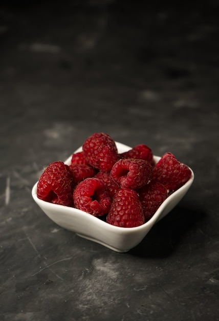 selektiver Fokus, saftige Himbeeren, Nahaufnahme, in einer weißen kleinen Vase auf einer dunklen Oberfläche