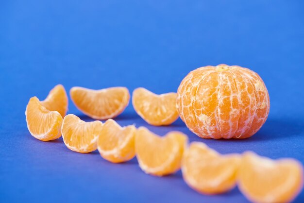 Selektiver Fokus von Mandarinenscheiben in der Nähe von geschälter Clementine auf blauem Hintergrund