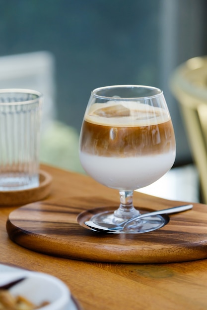 Selektiver Fokus, Weinglas Eiskaffee zwei Schichten frische Milch und Espresso kurz auf Holztisch im Café.