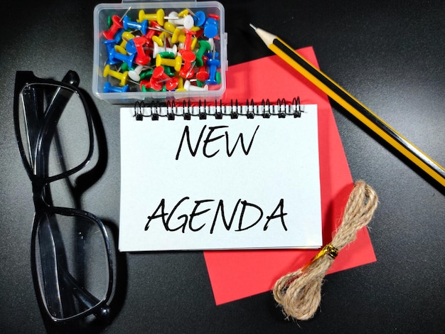 Selektiver FokusWord NEW AGENDA auf Notebook mit Pencilglassespincboard und Wurzel auf schwarzem Hintergrund