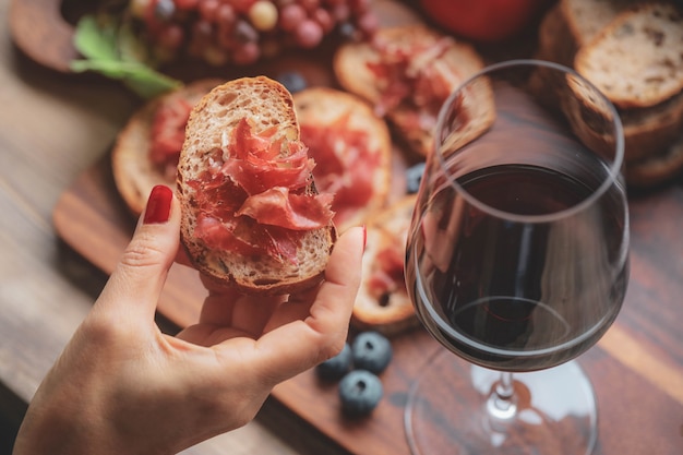 Selektives Foucs auf dem Finger, der Schinken jamon serrano und Gläser Rotwein auf hölzernem Brett hält