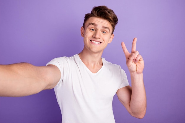 Selfie de apuesto joven fotógrafo blogueando hacer signo v fondo de color brillante aislado