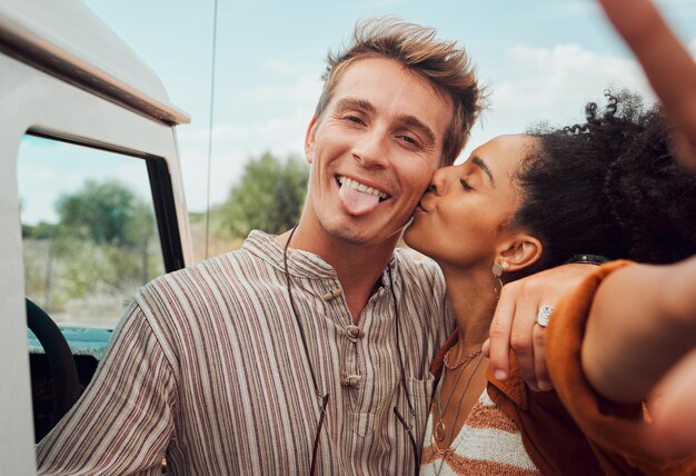Selfie beso y pareja tomando una foto en un viaje por carretera divirtiéndose juntos en una aventura de viaje Amor naturaleza y mujer negra besando a hombre para vínculo fotográfico en momento romántico en el campo