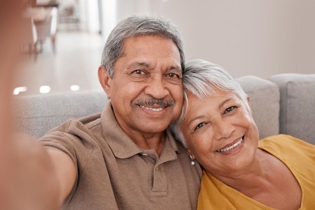 Selfie casal e amor com um homem e uma mulher sentados no sofá de sua casa juntos para uma fotografia Retrato de amor e sorriso com idosos aposentados tirando uma foto na sala de estar