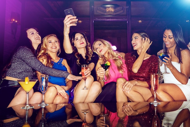 Selfie club y mujeres con bebidas en una fiesta para cumpleaños de año nuevo o celebración festiva Diversión social y amigos tomando fotos en un teléfono mientras beben bebidas alcohólicas en un club nocturno juntos