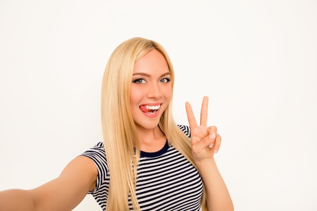 Selfie cómico de niña juguetona mostrando lengua y dos dedos