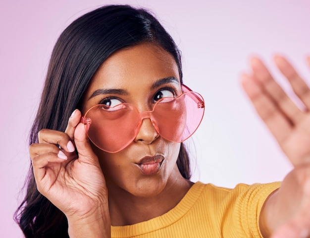 Selfie coração e óculos de sol por mulher indiana no estúdio emoji legal e divertido no fundo roxo Óculos moderno e influenciador da moda feminina da geração z posando para foto de perfil ou postagem no blog