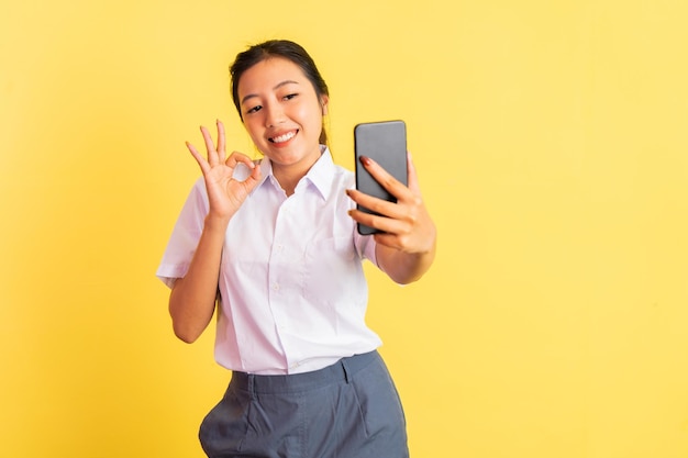 Selfie de colegial usando handphone com gesto de mão bem