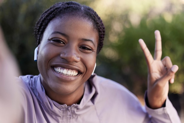 Selfie de fitness mulher negra feliz e sinal de paz com música para motivação de exercício, influenciador de blog de esportes e estilo de vida saudável, fotografia de smartphone ao ar livre, sorriso e treino matinal