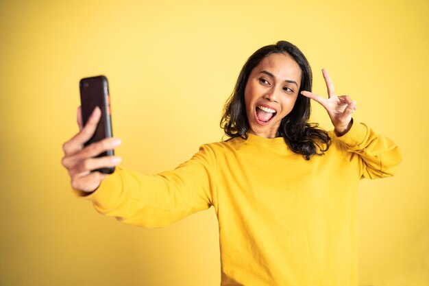 Selfie de jovem mulher usando a câmera do celular com sinal v