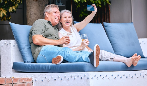 Selfie entspannen und älteres Paar mit einem Drink auf einem Sofa im Freien im Urlaub in Costa Rica Ruhestandsalkohol und glücklicher älterer Mann und Frau mit einem Telefon für Fotolächeln und Erinnerung an einen Urlaub