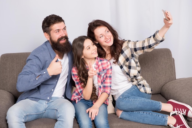 Selfie Familia feliz en casa Teléfono inteligente moderno Niña usa teléfono inteligente con madre y padre hombre barbudo y mujer con niño Selfie mania Familia hace selfie en teléfono inteligente Me encanta selfie