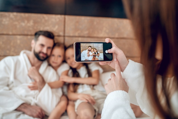 Selfie. Familie in weißen Gewändern, die im Bett liegen und Selfie machen