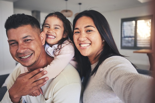 Foto selfie feliz y retrato de una familia con una sonrisa uniéndose en la sala de su casa. juntos aman y padres jóvenes felices tomándose una foto con su dulce niña para recordar recuerdos en casa
