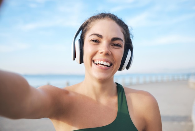 Selfie fitness e fones de ouvido femininos para treinamento ao ar livre, corrida ou exercício em videochamada para atualização de influenciadores Retrato musical e foto de perfil de esportista em exercícios de praia ou cardio