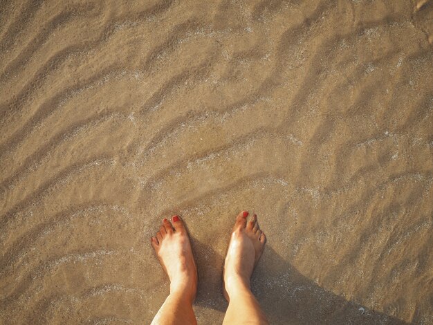 Selfie-Frauenfüße auf beige Sandsommersonnenuntergang setzen Hintergrund auf den Strand.