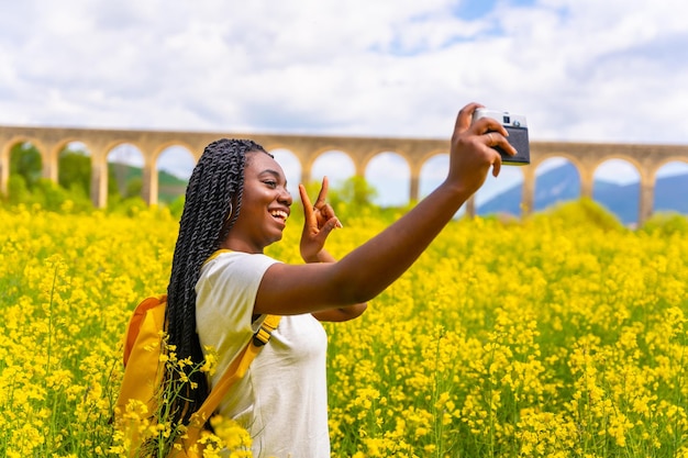 Selfie in der Natur mit einer Vintage-Kamera ein Mädchen schwarzer Ethnizität mit Zöpfen ein Reisender in einem Feld gelber Blumen