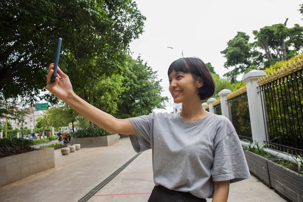 Selfie jovem asiática com celular em espaços públicos
