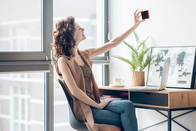 Selfie. Junge Frau, die nahe am Fenster sitzt und Selfie macht