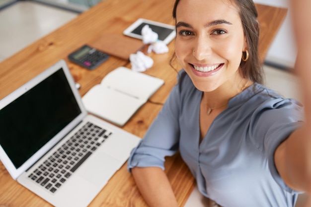 Selfie laptop e mulher feliz trabalhando na mesa do escritório para o sucesso da empresa de tecnologia da web inicialização digital e sorriso de funcionário no escritório Fotografia de smartphone gerente de seo e felicidade na mesa de trabalho