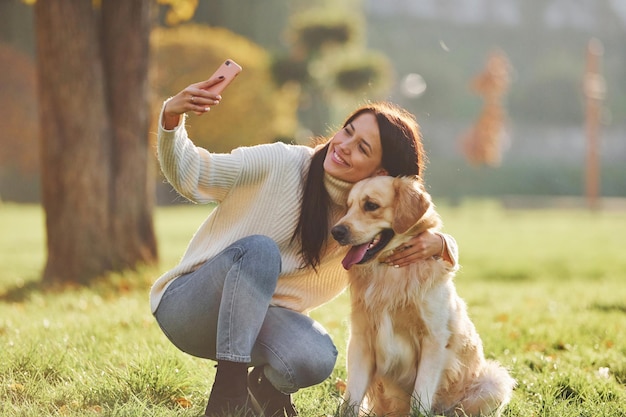 Selfie machen Junge Frau geht mit Golden Retriever im Park spazieren