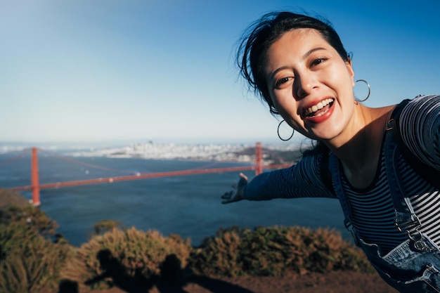 Selfie-Mädchen auf Reisen über die Goldene Brücke von San Francisco. Asiatische erwachsene Frau, die während der Sommerferien mit ihrem Smartphone fotografiert, zeigt die berühmte amerikanische Attraktion Kalifornien USA.