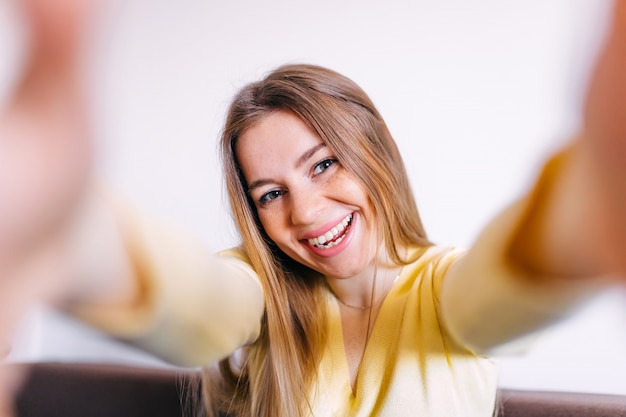 Foto selfie mania. cerca de feliz mujer morena con sonrisa radiante en traje amarillo tomando un autorretrato en su teléfono móvil