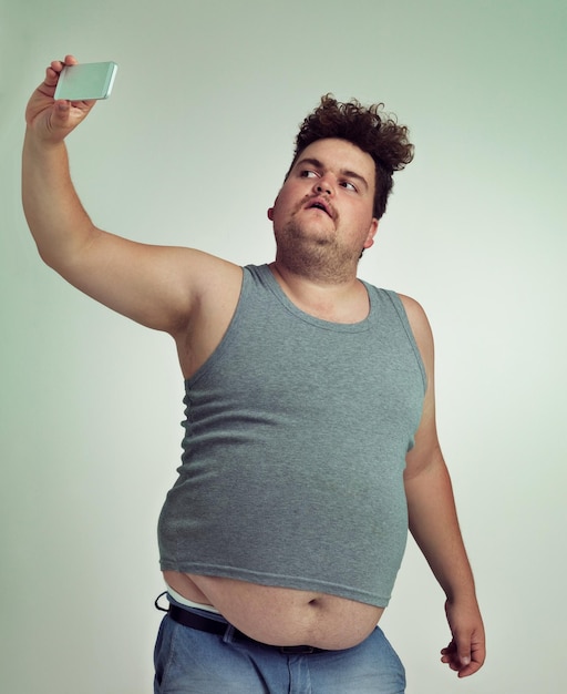 Selfie moda e homem de tamanho maior em estúdio posando com roupa casual elegante e legal com estômago Estilo pessoa masculina séria e louca com fotografia imagem isolada por fundo cinza