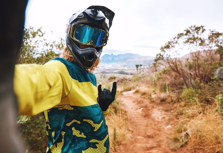 Foto selfie de motociclista deportivo y ciclismo en el campo natural o al aire libre signo de mano de roca bmx o autorretrato de ciclista en arena o camino de tierra para la memoria de aventuras o publicación de imágenes en línea en las redes sociales