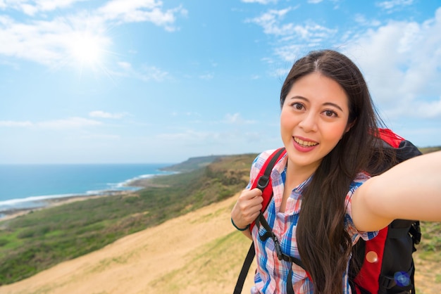 selfie mulher sorridente com equipamento de caminhada indo para o famoso país insular escalando a montanha e com belas paisagens tirando fotos durante as férias sobre copyspace em branco.