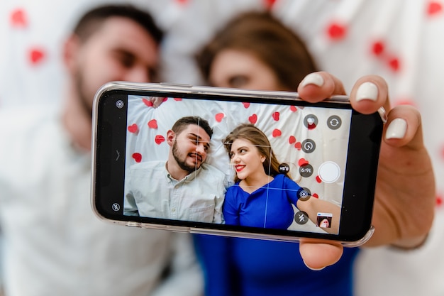 Selfie en la pantalla del teléfono del hombre y la mujer enamorados en la cama