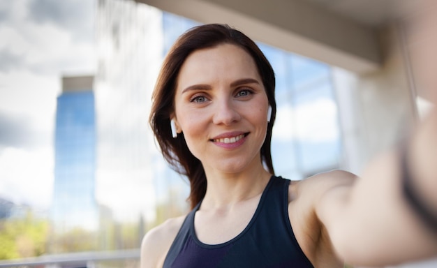 Selfie-Porträt einer süßen lächelnden Fitnessfrau mit Kopfhörern in der Stadt