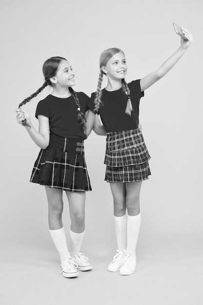 Selfie pose meninas pequenas fazendo selfie no telefone se divertindo irmandade e amizade feliz dia do conhecimento infância felicidade educação conceito de volta à escola rede social meninas de uniforme