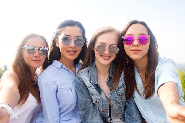 Un selfie de primer plano de grupos de mujeres en la naturaleza. Hermosas jóvenes estudiantes con coloridas gafas de sol sonríen y se regocijan ante la cámara