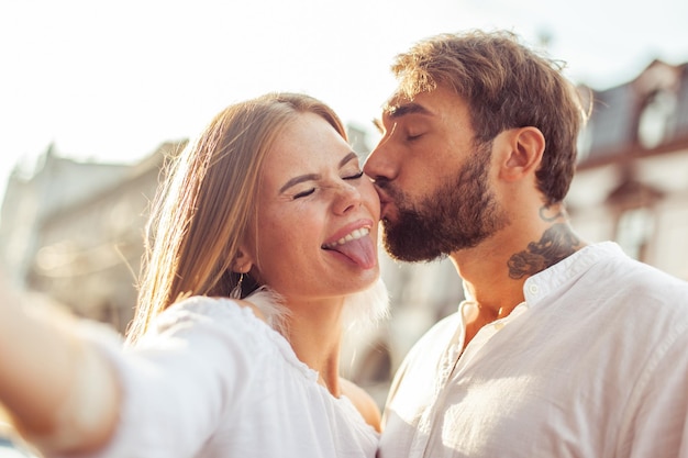 Selfie retrato de una joven pareja enamorada Hombre besa a su novia en la mejilla en la ciudad divirtiéndose