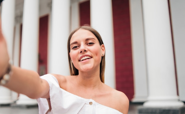 Selfie retrato de una mujer carismática alegre contra un edificio con columnas en el exterior