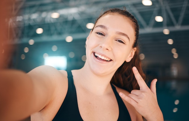 Selfie rock e retrato de uma garota em uma academia para corrida e saúde com um sinal para um treino Esportes felizes e rosto de uma garota com um emoji de mão de foto e sorriso para exercícios e esportes