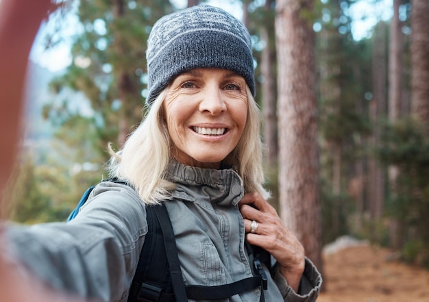 Selfie senderismo y una mujer mayor en el bosque para una aventura de fitness o la exploración de la naturaleza Viajes de retratos y ejercicio con una mujer madura excursionista en las montañas o bosques para una caminata