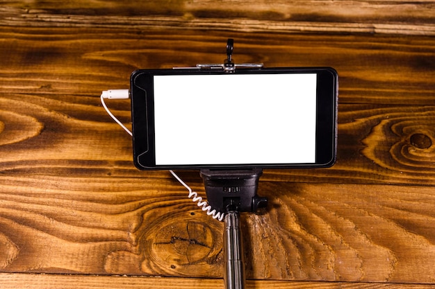 Selfie stick con smartphone moderno en una mesa de madera