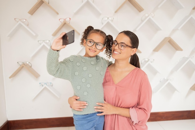 Selfie telefone e família com óculos de visão na loja de varejo para cuidados com os olhos e saúde de bem-estar Mãe, filho e sorriso para fotografia de mídia social de smartphone juntos em loja de optometria especializada