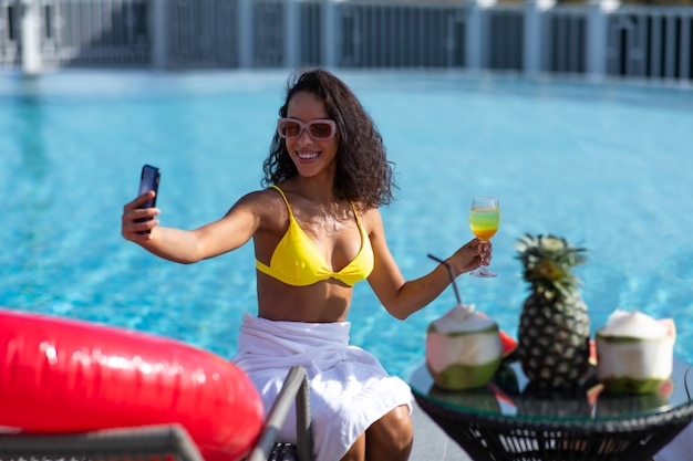 Selfie por teléfono inteligente. retrato de una atractiva chica morena selfie junto a la piscina.