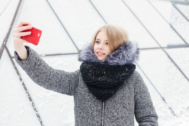 Selfie time, la joven bloguera funky está haciendo una foto para su página de redes sociales. Mujer joven feliz tomando selfie. Clima frío y soleado. Concepto de invierno de mujer.