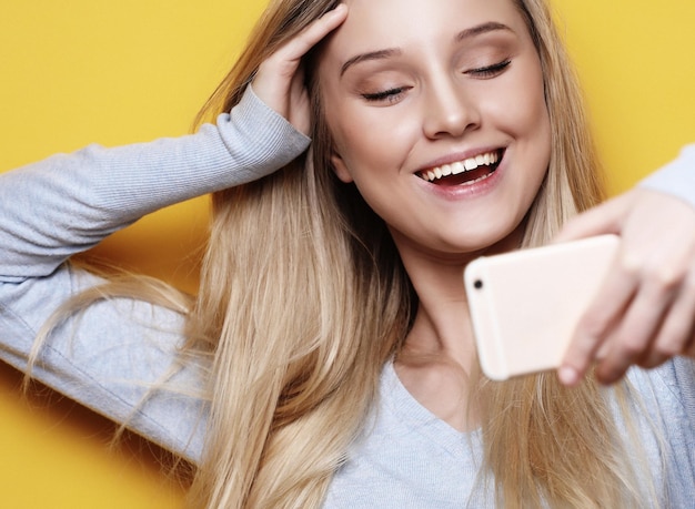 Selfie time Joven mujer rubia sonriente haciendo selfie sobre fondo amarillo