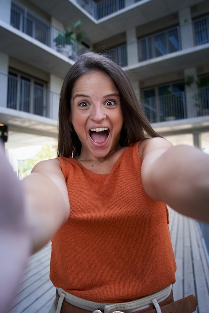 Selfie vertical de uma jovem com a boca aberta gritando de felicidade perto de pessoas