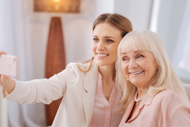 Selfie Zeit. Fröhliche positive entzückte Frauen, die lächeln und in eine Smartphone-Kamera schauen, während sie zusammen ein Selfie machen