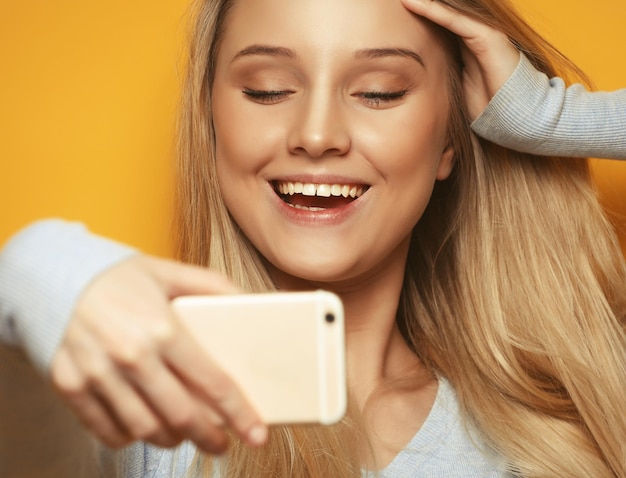 Selfie-Zeit Junge lächelnde blonde Frau macht Selfie auf gelbem Hintergrund