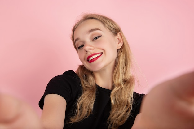 Selfie Zeit. Porträt der jungen emotionalen Frau, die lokalisiert auf rosa Studiohintergrund gestikuliert. Menschliche Emotionen, Gesichtsausdruck, Verkauf, Anzeigenkonzept. Blondes kaukasisches hübsches vorbildliches Gestikulieren. Exemplar.