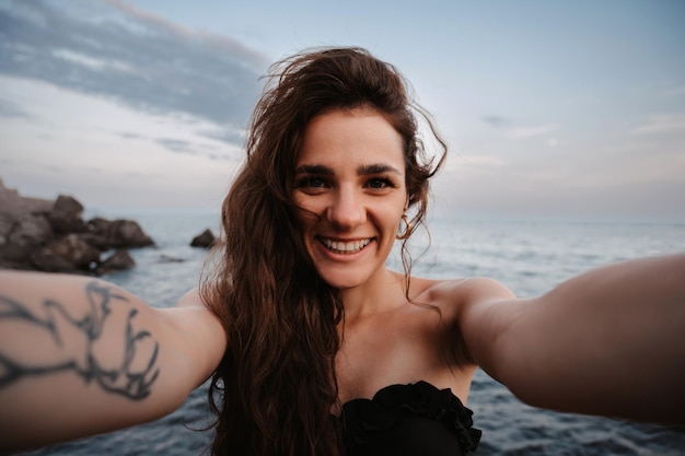 Selfieretrato de una chica atractiva con el pelo largo sonriendo a la cámara de pie contra el fondo del mar El concepto de vacaciones turísticas