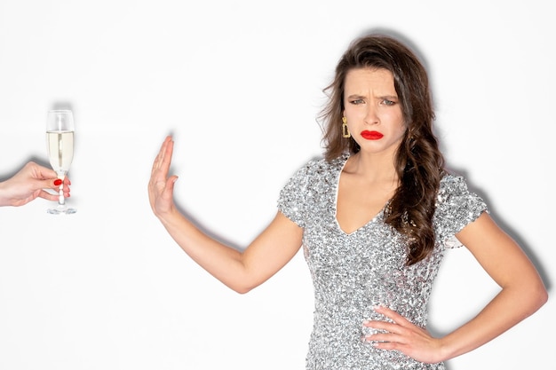 Sem álcool Mulher abstêmia Festa de aniversário Pare a celebração Senhora sombria em vestido prateado de lantejoulas recusando taça de champanhe posando espaço isolado em branco