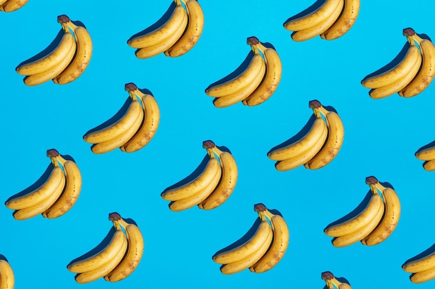 Foto sem costura fundo azul claro com padrão de bananas amarelas maduras e sombras escuras duras. nova tendência de cores 2021. conceito de cena mínima. imagem de frutas tropicais abstratas de arte pop. espaço de cópia grátis.